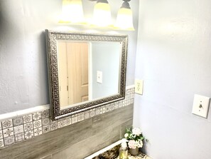A bathroom with a large mirror, decorative tiles, and a sink with a vase of flowers.