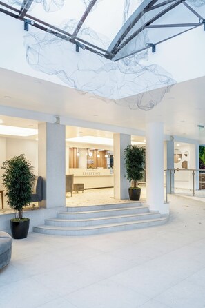 A hotel reception area with a modern design, featuring a reception desk, seating area, and a staircase leading to the upper floor. - Grand Sunny Beach (Nessebar)