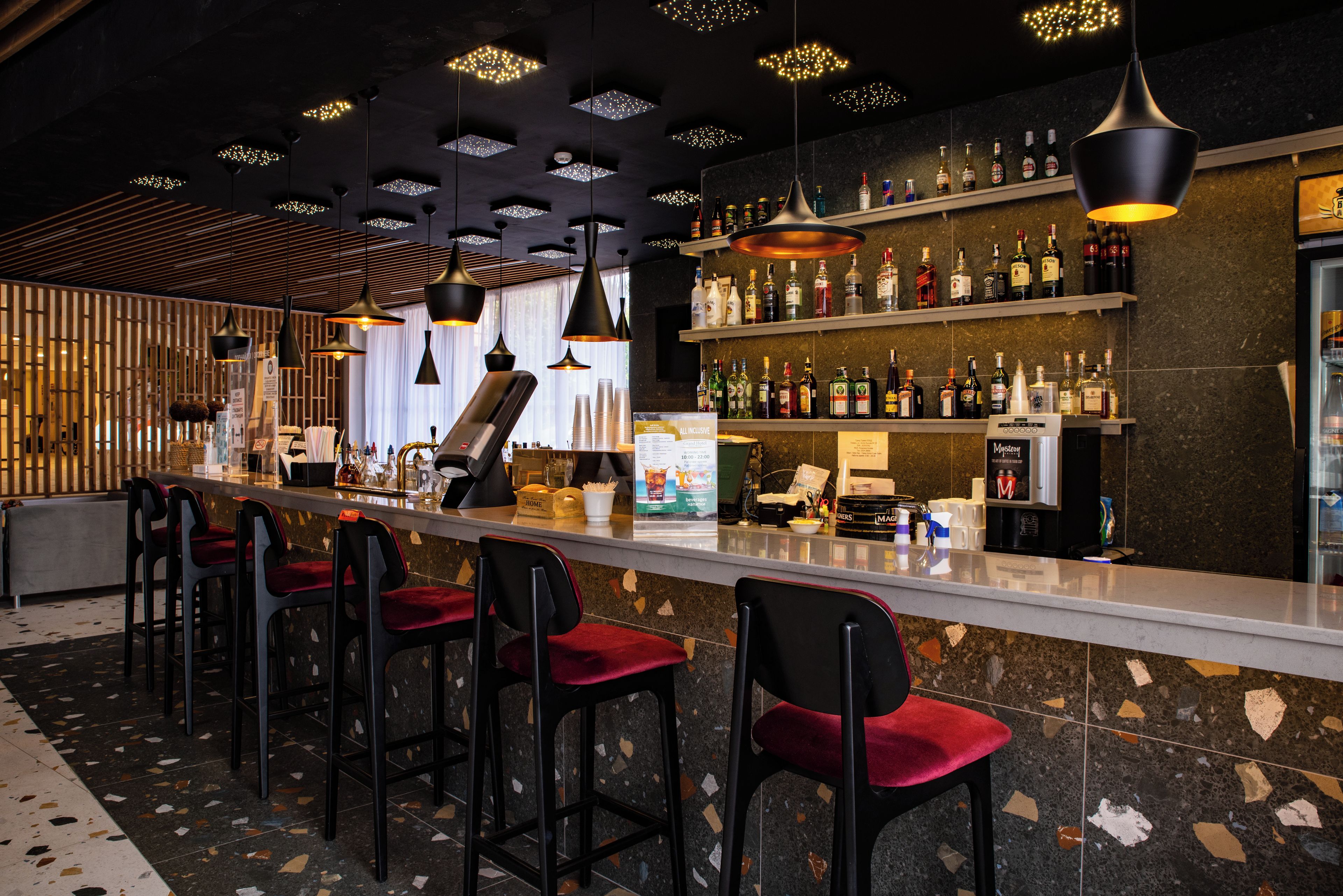Zona de bar con una barra larga, diferentes opciones de asiento y una variedad de botellas en estanterías.