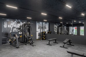 Une salle de sport équipée de machines d’exercice, de bancs et d’un mur recouvert de miroirs.