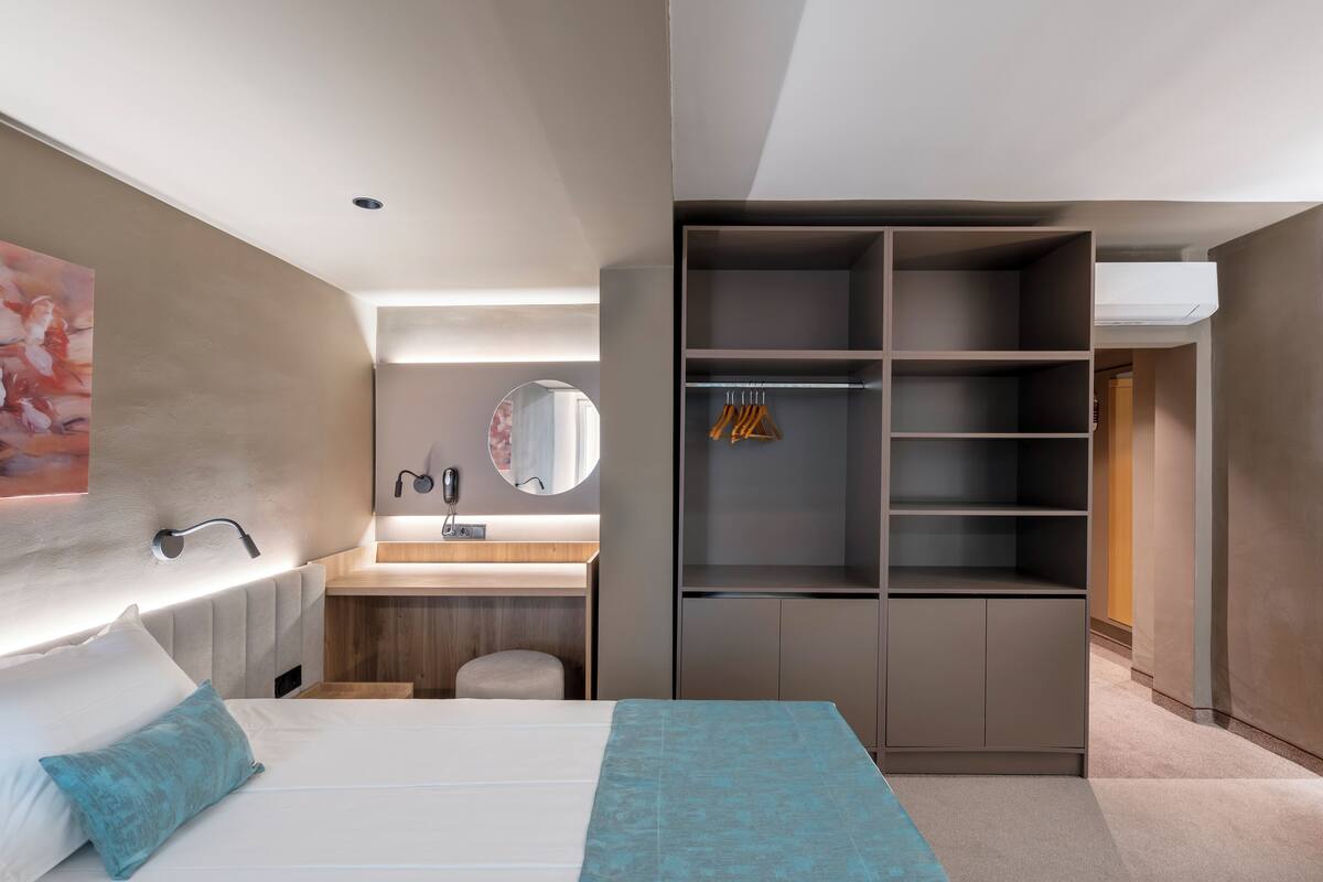 A modern hotel room with a bed, a bedside table, a mirror, a wardrobe, and a bathroom area.