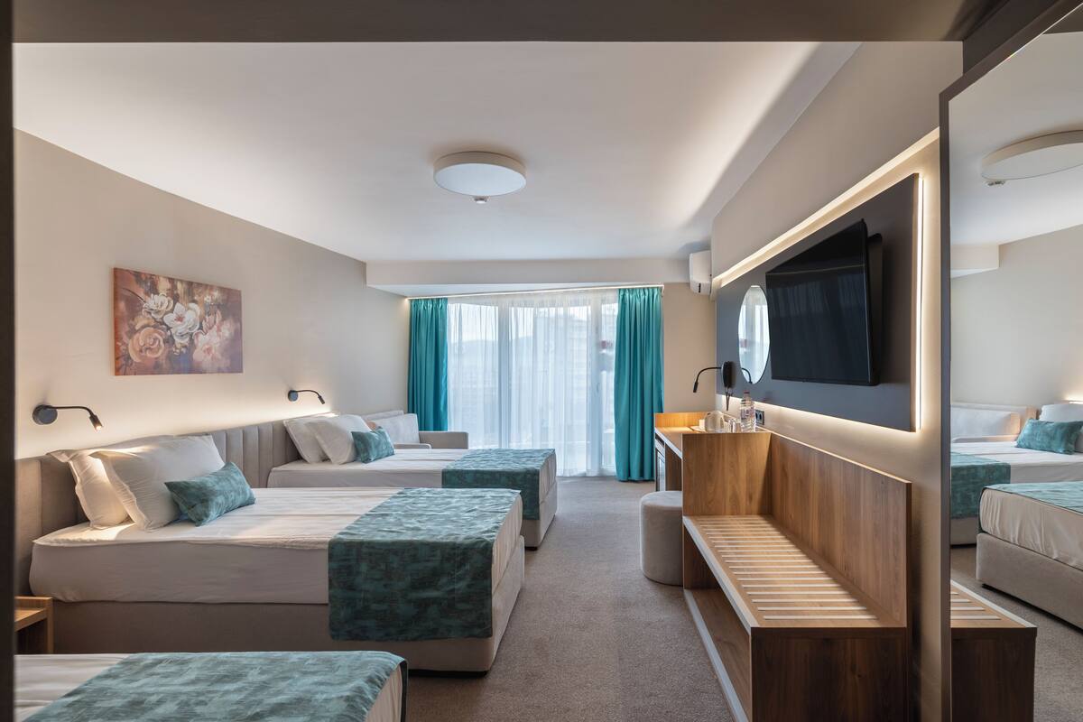 A hotel room with two beds, a wooden bench, a TV, and a large mirror.
