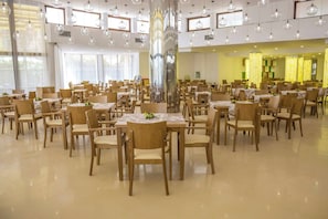 A spacious dining area with multiple tables and chairs, large windows, and hanging light fixtures. - Grand Sunny Beach (Nessebar)