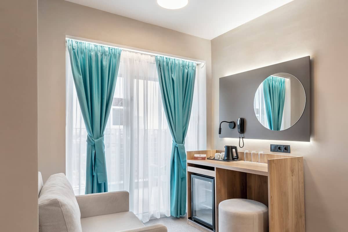 Una habitación de hotel moderna con sofá, un escritorio pequeño con espejo, cafetera y mini refrigerador.