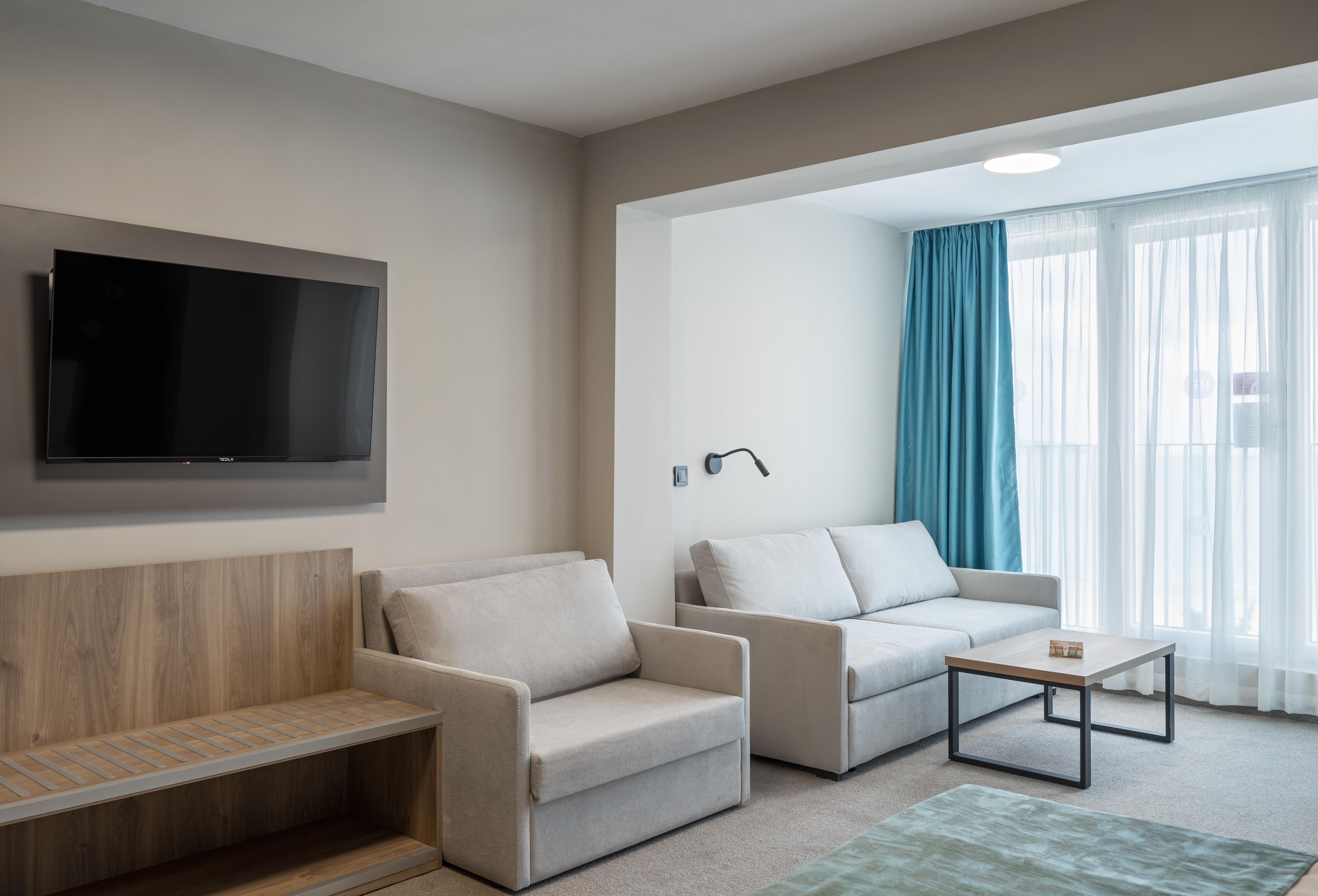 A modern living room with a flat-screen TV, two sofas, a coffee table, and a wooden bench.