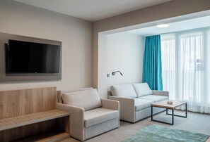 A modern living room with a flat-screen TV mounted on the wall, two sofas, a coffee table, and a wooden bench. - Grand Sunny Beach (Nessebar)