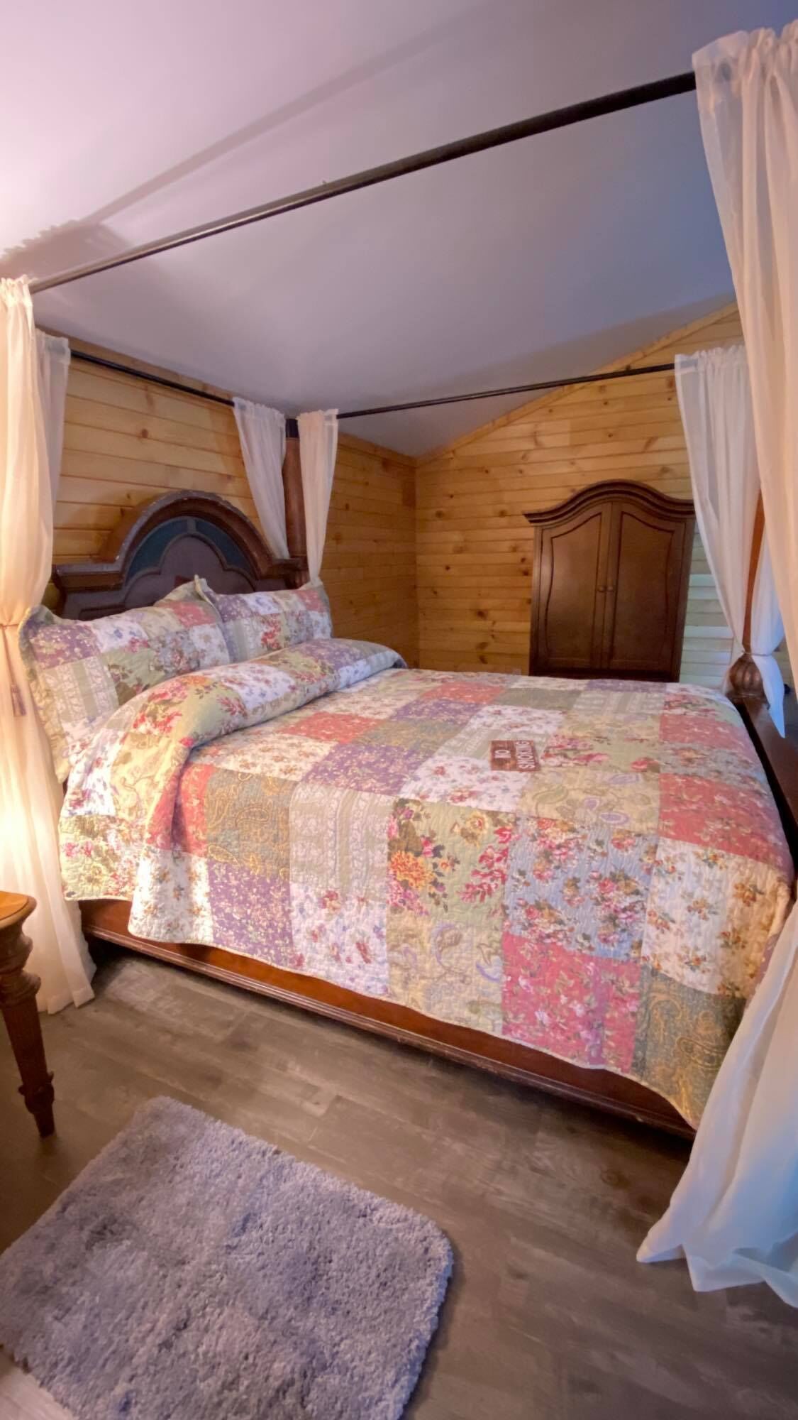 Une chambre dans une cabane en bois, avec un lit, des rideaux et un petit tapis.
