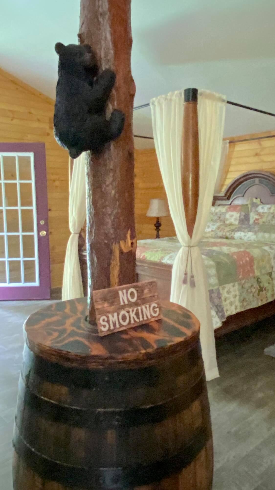 A bear climbing a tree in a room with a 'NO SMOKING' sign on a barrel.
