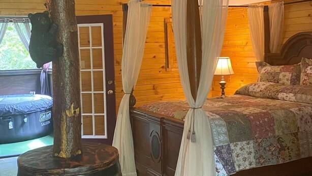 A rustic wooden room with a four-poster bed, a large barrel, and a door with a window. - Hot Tub, Fire Ring, Charcoal Grill, Hocking Hills, Buckeye Lake, Legend Valley (Somerset)