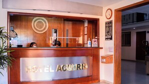 A hotel reception desk with a wooden finish and a glass panel displaying the hotel name. - Hotel Acuario  (Ocotlan)
