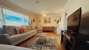 Een woonkamer met een bank, fauteuil, salontafel, televisie en een kamerkleed met dessin.