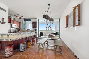 A kitchen with a large island, wooden cabinets, and a ceiling fan. There are various kitchen appliances and a view of the outside.