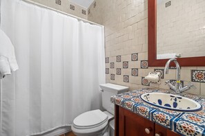 A bathroom with a white toilet, a shower curtain, a sink with a decorative tile backsplash, and a mirror above the sink.