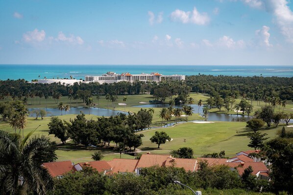 A golf course with a large building in the background, surrounded by palm trees and water features.