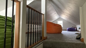 Un dormitorio tipo loft con techo inclinado, una escalera de madera, un sillón de peluche verde y un sillón de peluche morado.