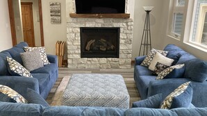 Una sala de estar con dos sofás azules, una chimenea de piedra, un televisor de pantalla plana encima y una lámpara de pie alta.
