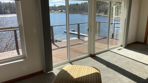 Una habitación con un amplio ventanal corredero que da a una terraza con vistas a un lago, una cama y un radiador.