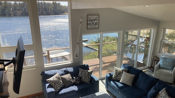 Una sala de estar con un ventanal que da a un lago, un sofá azul y un cartel que dice 'HAPPY HOUR en el lago'.
