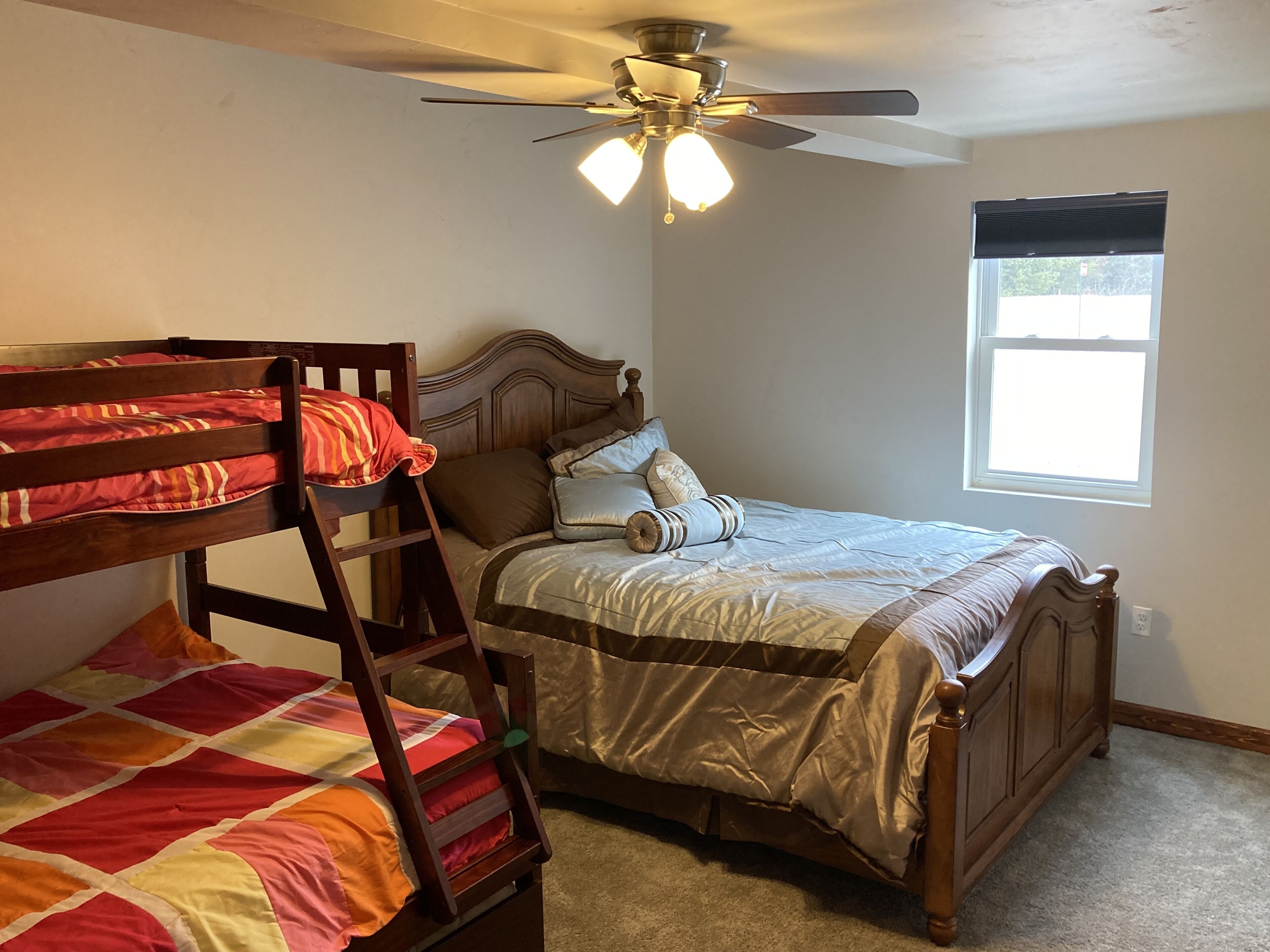 A bedroom with a bunk bed, a single bed, a ceiling fan, and a window.