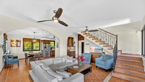 A spacious living room with a large sectional sofa, a dining area with a wooden table, and a staircase leading to an upper level. - Casa D'Palma-steps to Sandy Beach! (Rincón)