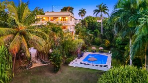 A large house with a swimming pool surrounded by lush greenery and palm trees. - Casa D'Palma-steps to Sandy Beach! (Rincón)
