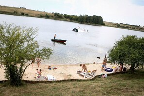 Une plage au bord d’un lac, où l’on voit des gens se détendre, un petit bateau et une rive bordée d’arbres.