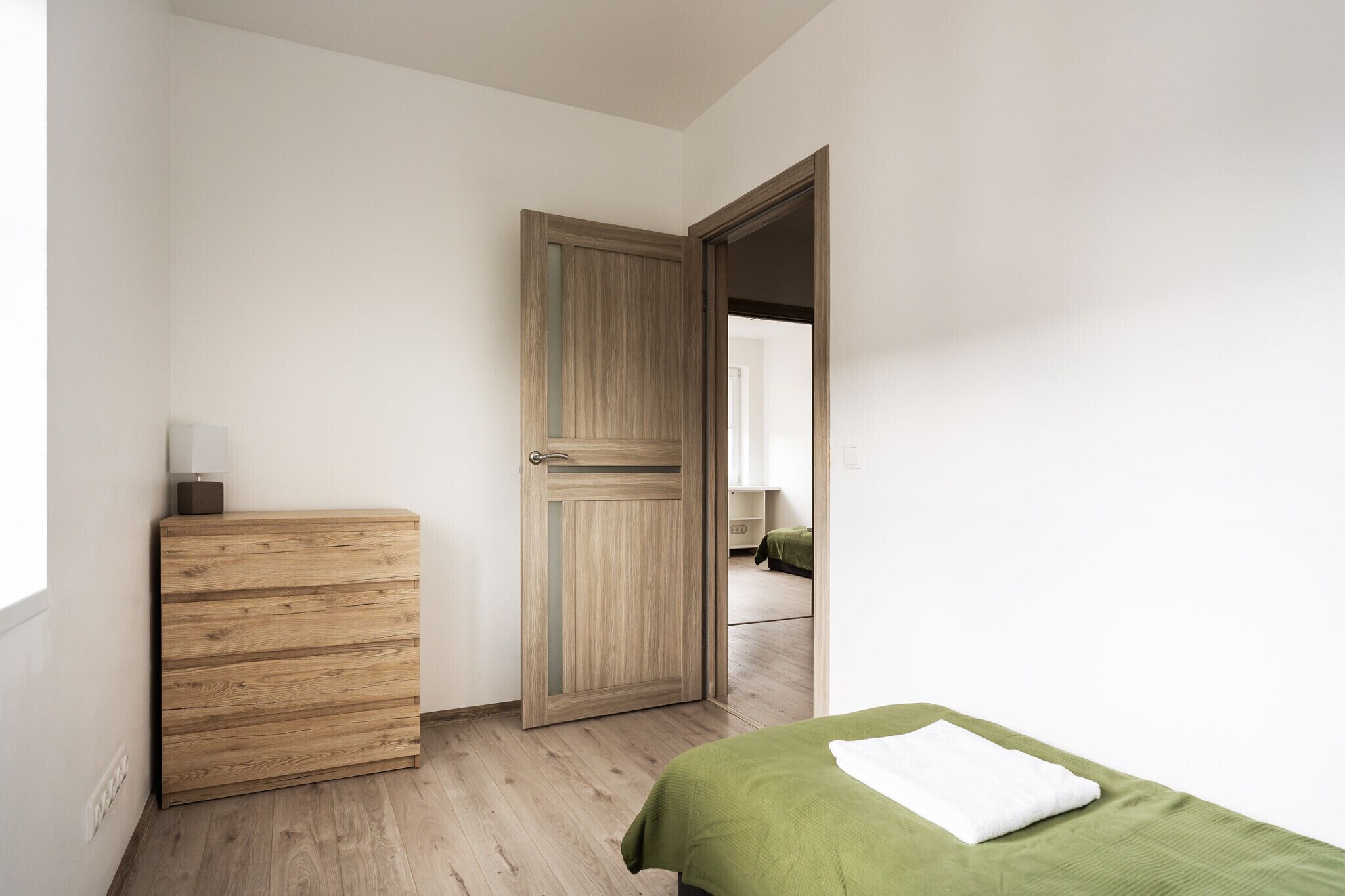 A bedroom with a wooden dresser, a green bed, and a door leading to another room.
