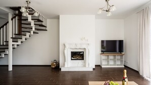 A modern living room with a staircase, fireplace, flat-screen TV, and a bottle of champagne on a table. - 2 House Between two lakes (Vilnius)