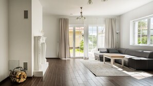 A modern living room with a dark wood floor, a grey sofa, a white coffee table, and a large window with curtains. - 2 House Between two lakes (Vilnius)