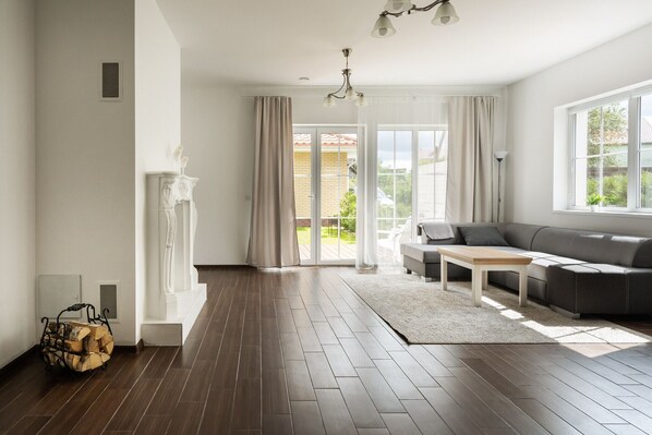 A modern living room with a dark wood floor, a grey sofa, a white coffee table, and a large window with curtains. - 2 House Between two lakes (Vilnius)