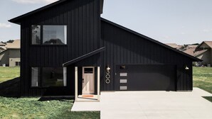 Een modern huis met twee verdiepingen, een zwart uiterlijk, een zichtbare garage deur en een voordeur met een klein portaal.