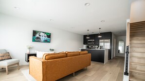 Een moderne woonkamer met een bank, een eethoek en een keuken met donkere kastjes en roestvrijstalen apparatuur.