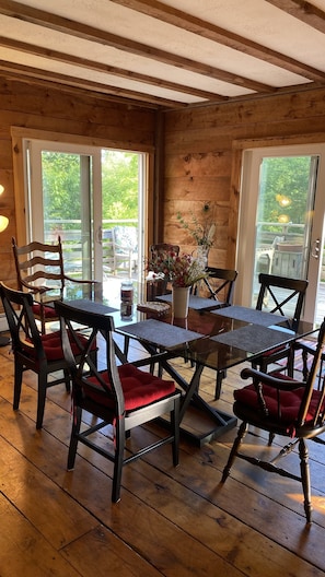 A wooden interior with a glass table surrounded by chairs with red cushions. - Mountain Top Escape (Putney)