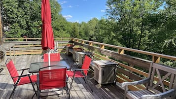 A wooden deck with outdoor seating, including tables and chairs, and a wooden railing.