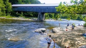 A covered bridge over a river with people near the water.