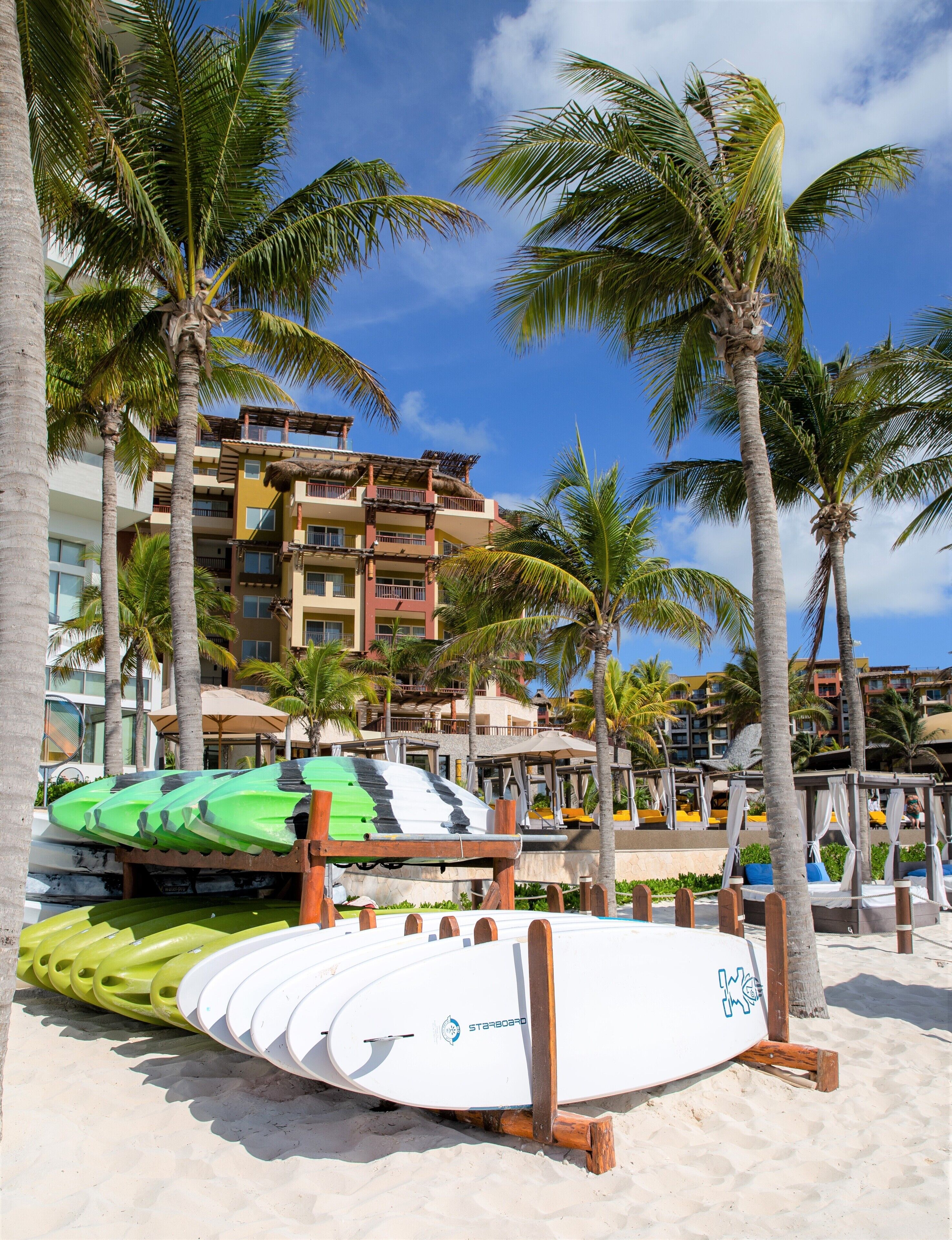 A beach with surfboards, palm trees, and a hotel building in the background.