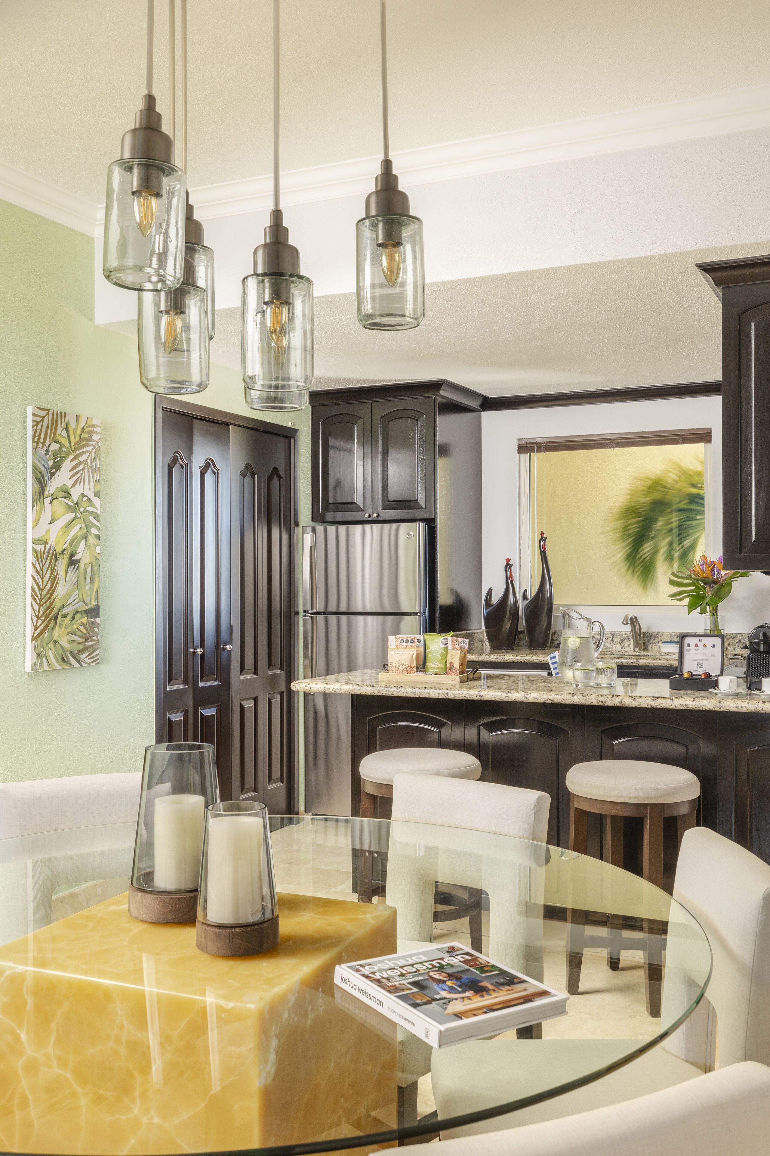 A modern kitchen with dark cabinets, a stainless steel refrigerator, and a glass dining table with candles.