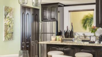 A modern kitchen with dark cabinets, a stainless steel refrigerator, and a glass dining table with candles.