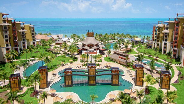 Un resort con varias piscinas, palmeras y vistas al océano.