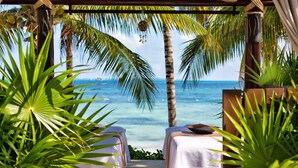 Un spa frente al mar con dos camillas de masaje bajo una pérgola de madera, con vistas al océano.