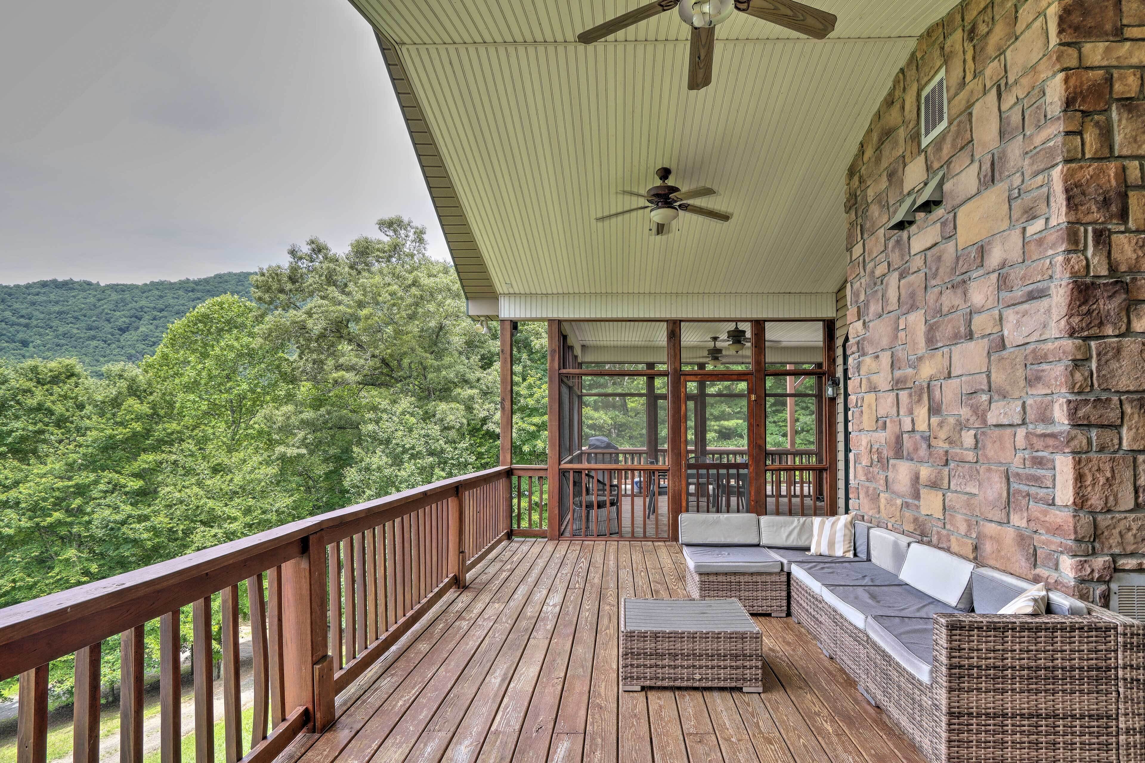 A wooden deck with wicker furniture, a stone wall, and a view of a forested hillside.