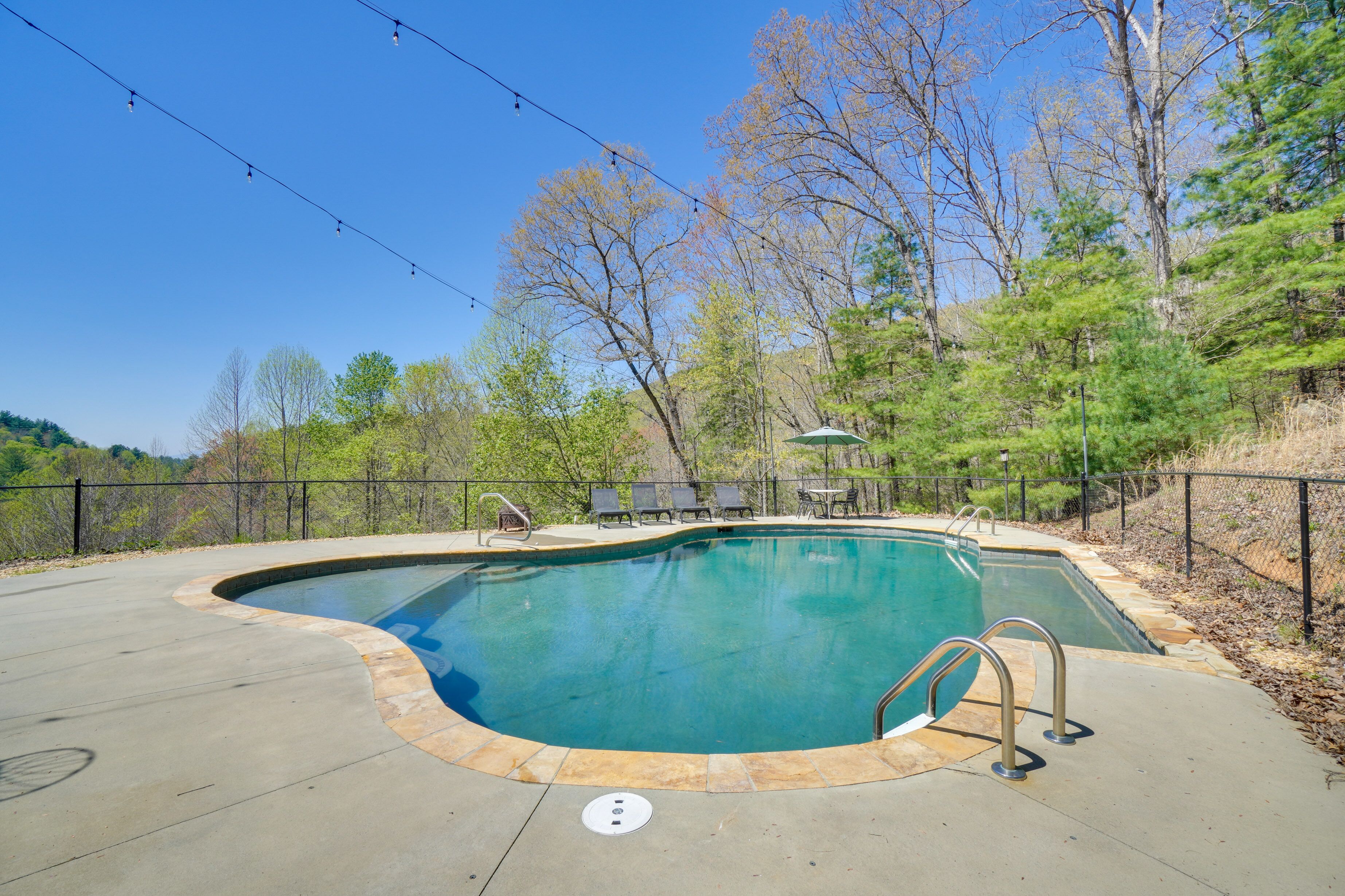A swimming pool with a curved edge, surrounded by a concrete deck and a metal fence.