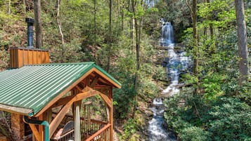 Une cabane en bois, surmontée d’un toit vert, qui surplombe une cascade au cœur d’une forêt.