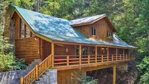 Eine Blockhütte mit Balkon, Steintreppe und einem Metall-Dach.