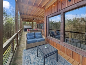 Eine überdachte Terrasse im Freien mit einer Couch, einem Tisch und großen Fenstern mit Blick auf einen Wald.