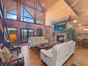 Un intérieur de chalet spacieux avec une cheminée, des murs en bois, un grand téléviseur et un coin salon confortable.