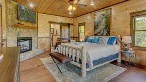 Ein Schlafzimmer einer Holzhütte mit einem Bett, einer Bank, einem Kamin und einem Waldgemälde.
