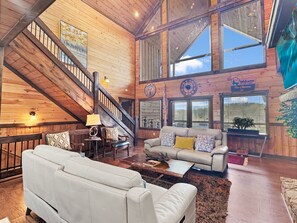 Geräumiges Cabin-Interieur mit hoher Decke, Holzwänden, einer Treppe, einer Sofagarnitur und einem großen Fenster mit Blick.