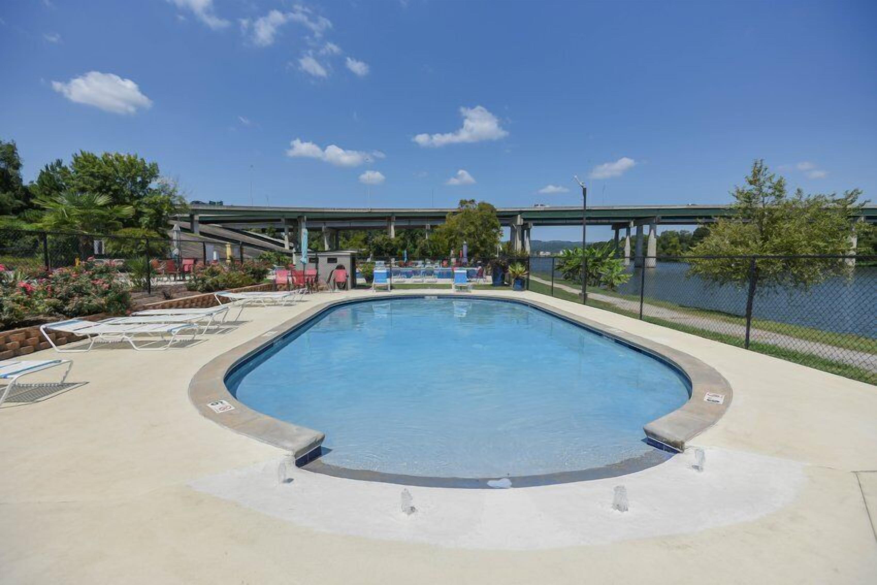Une piscine avec des chaises longues, un pont en arrière-plan et une étendue d’eau.