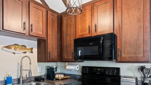 A kitchen with wooden cabinets, a black microwave, a stove, and a hanging light fixture. - Dockside at River Rocks Landing (Gadsden)